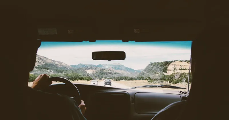 Conductor al volante de un coche por una carretera de montaña vista desde el asiento trasero